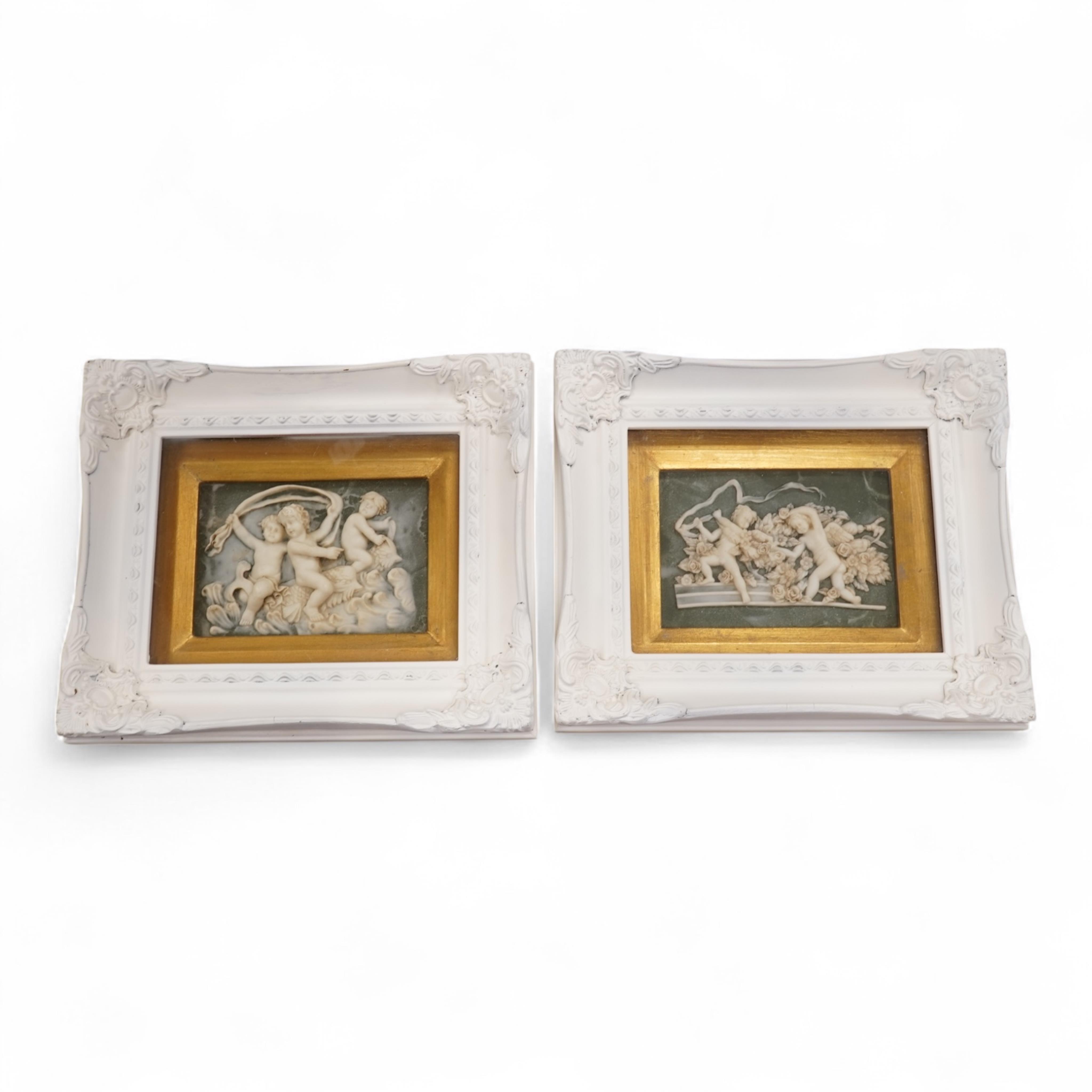 A pair of modern framed carved wax plaques of putti, housed in decorative painted frames, 27 x 32cm